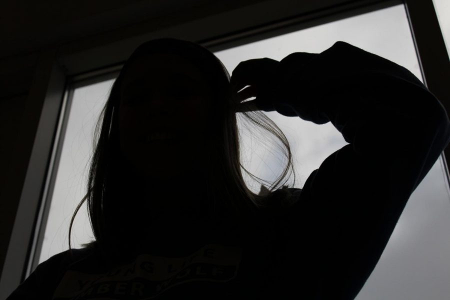A student embracing being alone by posing in front of a window with a dark shadow outline of the student. 