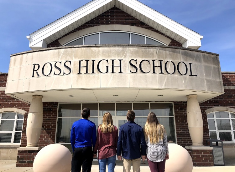 Four senior students hold hands and look at the front of Ross High School. 