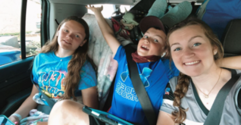 Gracie Elliott smiling beside her sister Sam, and her brother Tucker while driving to a softball tournament. 