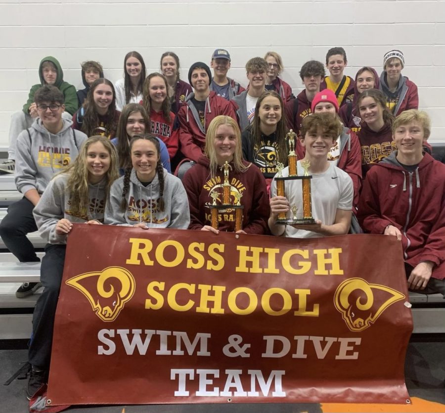 The 2021-22 RHS swim team poses for a picture on the RHS bleachers holding a maroon banner. 