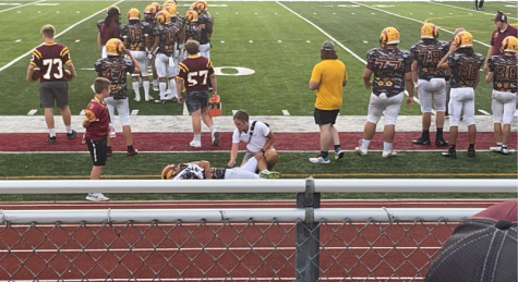Abigail Mathews helps a football player stretch his leg during a football game.