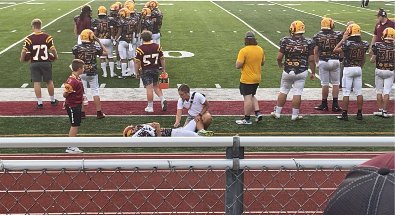 Abigail Mathews helps a football player stretch his leg during a football game.
